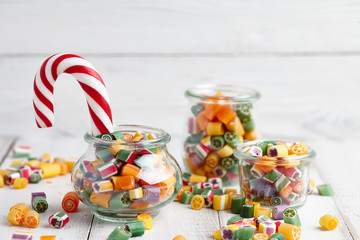 Colorful lollipops and candy canes in glass jars on white wooden background