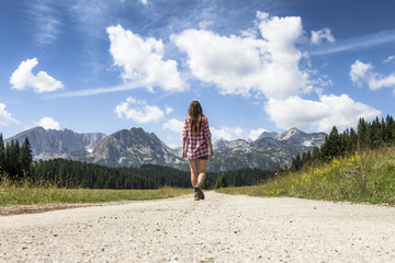 Naklejka premium Mountain road to freedom - Young girl freely walking to the beautiful mountain landscape