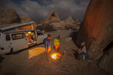 Three friends gathered around a fire near their camper van in Joshua Tree National Park, California.