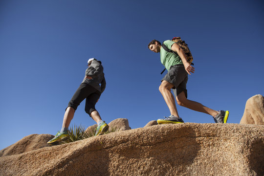 A man and woman hiking along a boulder in Joshua Tree National Park, California.