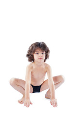 Obraz premium The curly-haired boy in a bathing suit sits in a pose of a frog looking at the camera. Blue background.