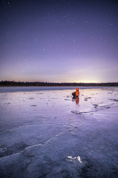 Person sitting on ice looking at stars, Finland 