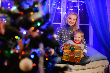 Fototapeta na wymiar mother and son smiling with Christmas present in hands on the background of Christmas lights and Christmas tree.