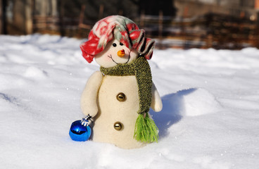 funny snowman in a hat with Christmas toys on a background of snow drifts