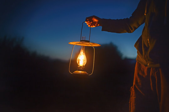 man holding the old lamp with a candle outdoors. hand holds a large lamp in the dark. ancient lantern with a candle illuminates the way on a night