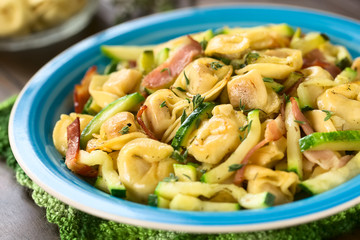 Gebackene mit Käse gefüllten Tortellinis mit Zucchini, Speck und Thymian, fotografiert mit natürlichem Licht (Selektiver Fokus, Fokus in die Mitte des Gerichts)