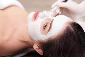 Spa concept. Young woman with nutrient facial mask in beauty salon, close up