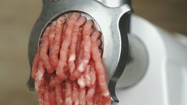 The making of ground beef using the electric meat grinder indoors. Close up