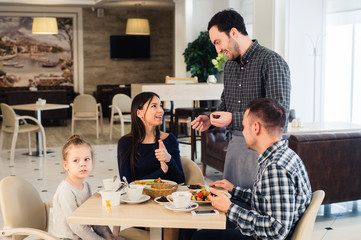 Friendly smiling waiter taking order at table of family having dinner together