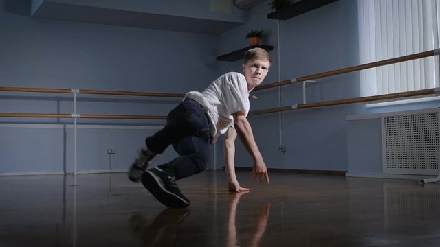 Talented dancer performs complex acrobatic movements of breakdance. Performances of dance on the floor in a spacious dance studio.