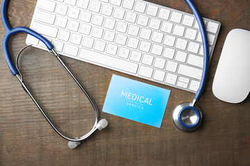 Business card, keyboard and stethoscope on wooden background. Medical service concept
