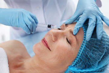 Senior woman having hyaluronic acid injection at beauty salon
