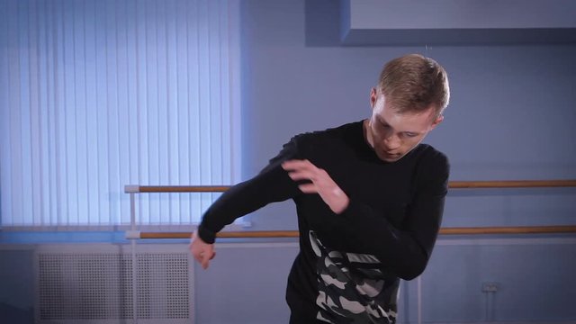 Close up of young hip-hop dancer in black trousers and pullover performing urbanstyle and streetdance in the room. Stundent of dancing school is executing modern freestyle and breakdance.