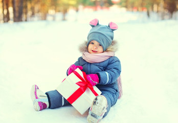 Winter happy little child with christmas red box gift sitting on