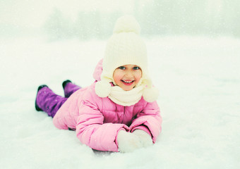 Fototapeta na wymiar Winter happy smiling little girl child playing lying on snow