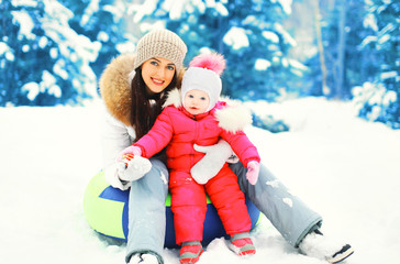 Winter happy smiling mother and child sitting on sled in snowy d