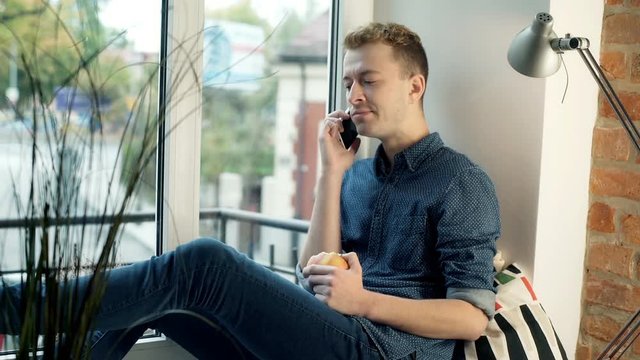 Happy rad haired man chatting on cellphone and eating apple
