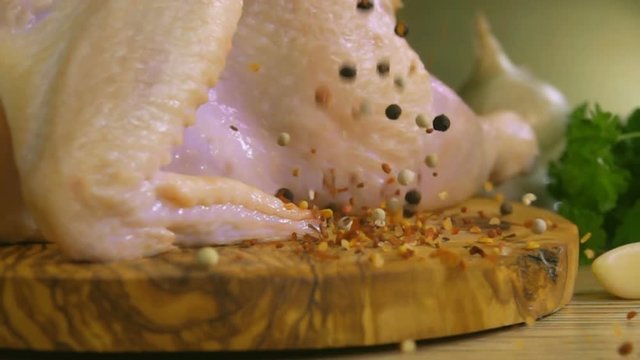 Spices are falling on a wooden board with raw chicken