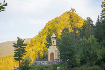 A small Christian chapel stands on the shore of forest lake.