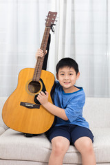 Happy Asian Chinese little boy playing guitar on the sofa