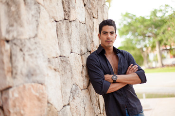 Obraz premium Latino male model standing with arms crossed against wall with unbuttoned shirt outdoor
