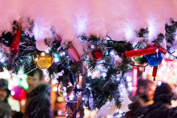 christmas decorations on fir-branches covered in snow with blurred christmas fun-fair on background