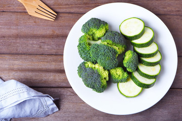 Top view of a healthy plate of fresh green broccoli and sliced zucchini.