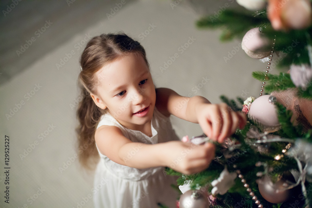 Wall mural cute little girl in dress decorating christmas tree