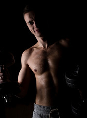 Handsome athletic man with dumbbell on a darck background