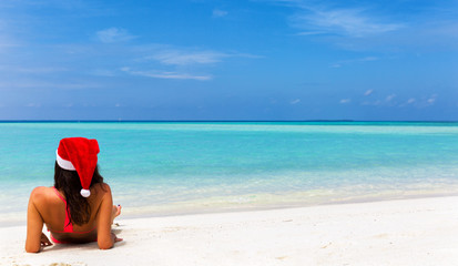 Fototapeta na wymiar Attraktive Frau mit Weihnachts Hut liegt am tropischen Strand