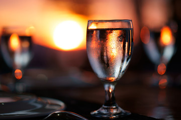 glass of water on the table with beautiful, colorful sunset at background