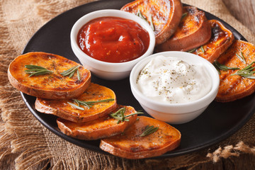 roasted sweet potatoes with rosemary served with sour cream and ketchup closeup. Horizontal