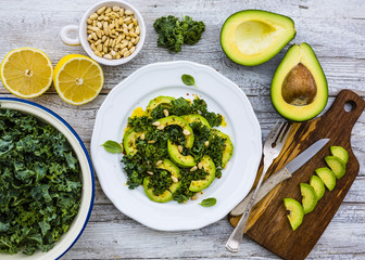 Fresh salad with kale leaves and avocado on a white plate on wooden table.