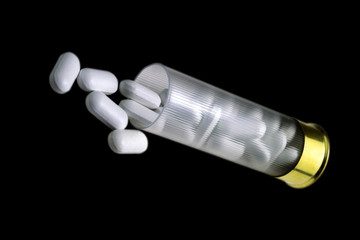 Concept of medical pills side effects. Transparent plastic Shotgun 12 caliber shell full of white antibiotic pills. Several pills outside the shell. Black background.