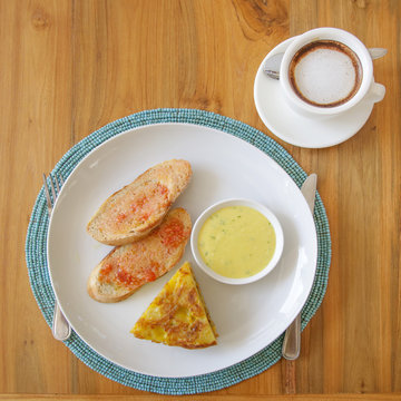 Spanish potato tortilla, bread and sauce served on the plate with a cup of coffee aside
