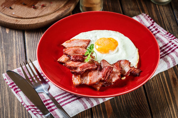 Slices of smoked bacon and fried egg on a red plate