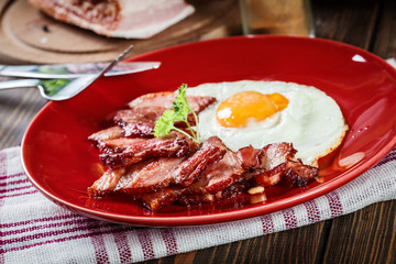 Slices of smoked bacon and fried egg on a red plate
