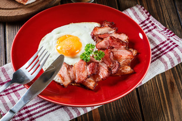 Slices of smoked bacon and fried egg on a red plate