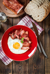 Slices of smoked bacon and fried egg on a red plate