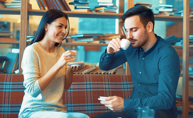 Young couple drinking coffee in cafeteria, surrounded with books