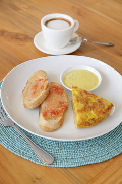 Spanish potato tortilla, bread and sauce served on the plate with a cup of coffee aside
