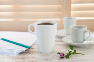Office workplace with  coffee cup on wooden desk table in front of window with blinds, selective focus