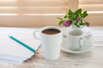 Office workplace with  coffee cup on wooden desk table in front of window with blinds, selective focus