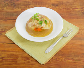 Pork jelly in white dish and fork on wooden surface