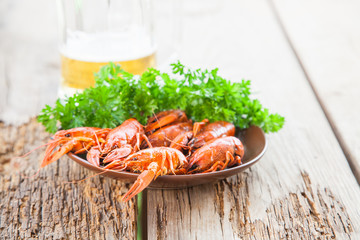 Boiled red crayfishes with a beer and green vegetables on a wooden rustic table. Close up. Selective focus.