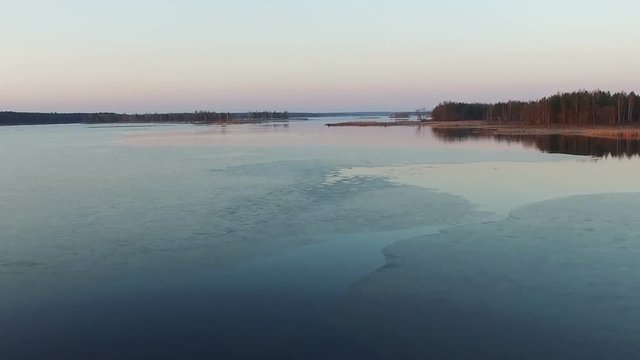 Low flight over wild frozen lake in winter on sunset, aerial view.
