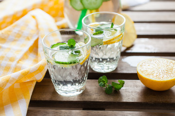 the refreshing drink with a lemon, a cucumber and rosemary in a glass on a table, selective focus