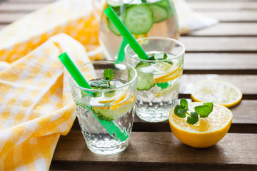 the refreshing drink with a lemon, a cucumber and rosemary in a glass on a table, selective focus