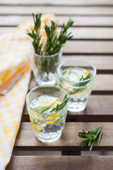 the refreshing drink with a lemon, a cucumber and rosemary in a glass on a table, selective focus
