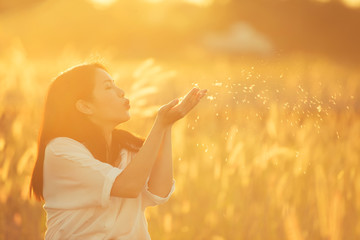 lifestyle concept - beautiful happy woman enjoying fresh air in field and blowing flower.